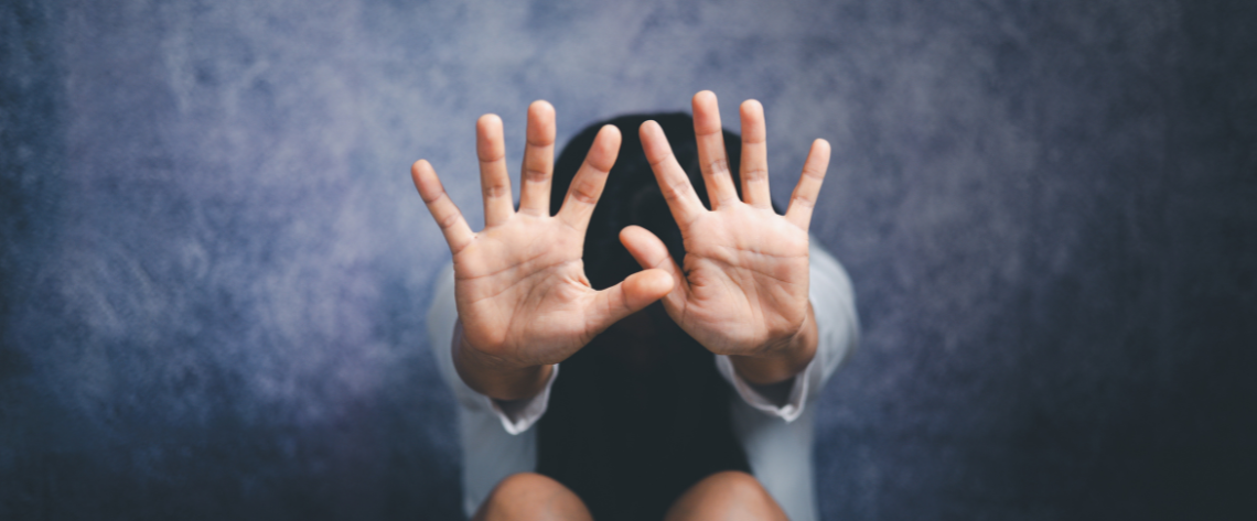 Auf dem Boden kauernde Frau schützt sich mit erhobenen Händen